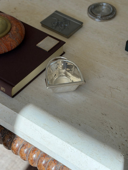 Ralph Lauren stirrup nut bowl on the corner of a travertine table among a brown book, pewter box, and chain rimmed coaster