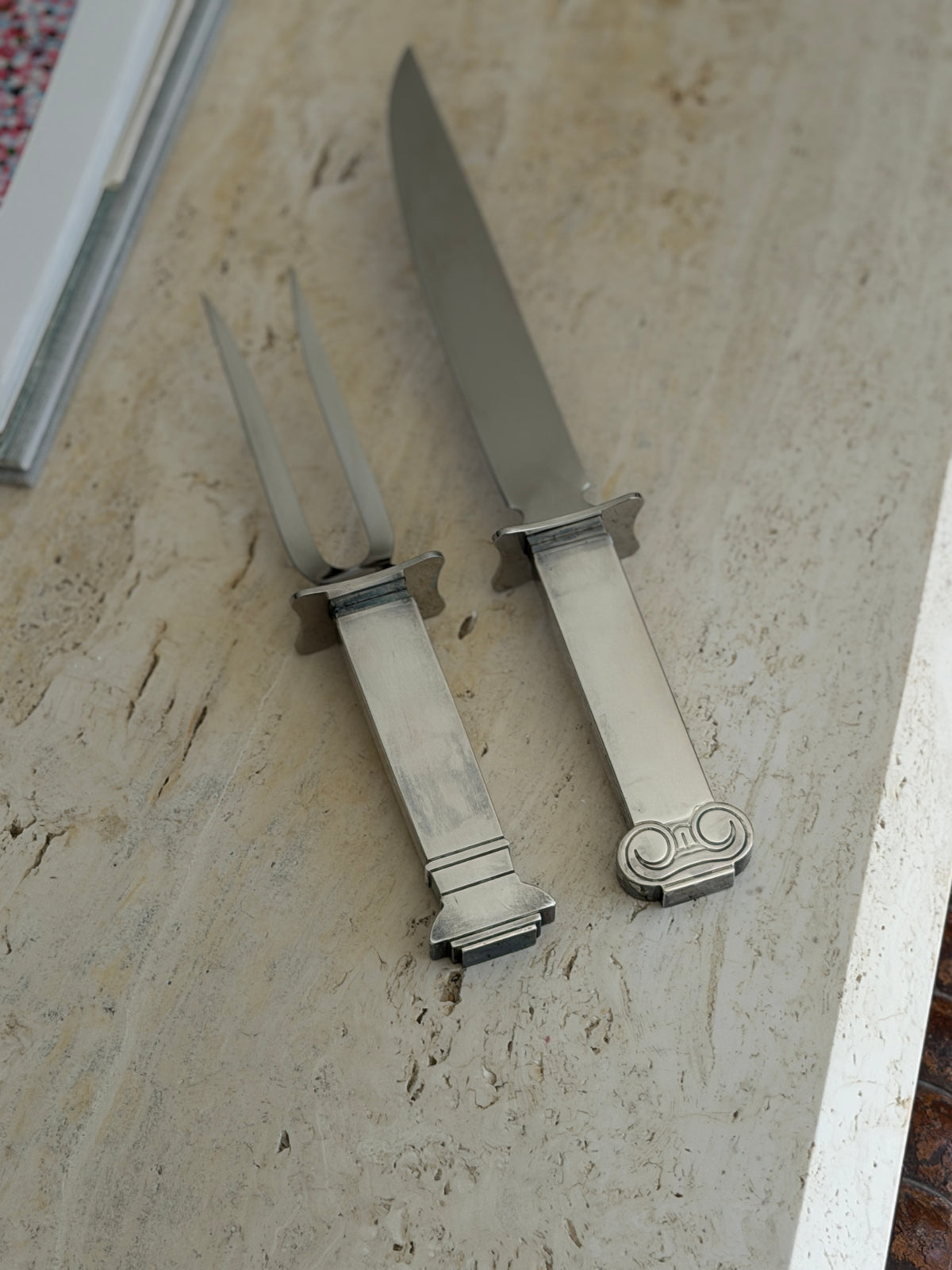 Carving knife and two tine fork from the Venturi set side by side, the knife handle capped with an Ionic scroll and the fork handle ending in a stepped base