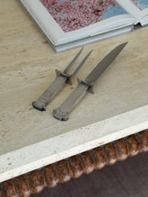 Swid Powell column carving set on a travertine console with a carved wood bobbin edge below and an open art book behind