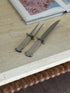 Swid Powell column carving set on a travertine console with a carved wood bobbin edge below and an open art book behind