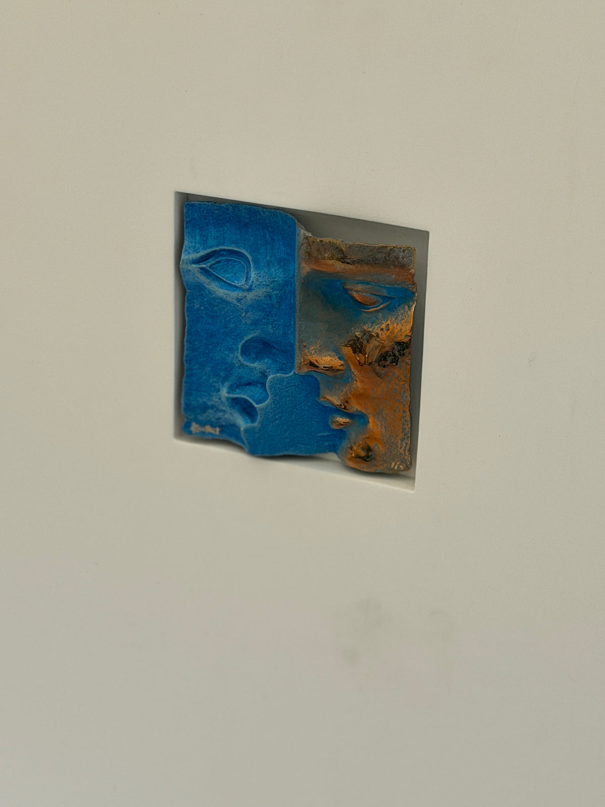 Rene Berthet bronze relief of two overlapping faces, one in textured cobalt blue patina and one in burnished copper bronze, set into a white shadowbox window