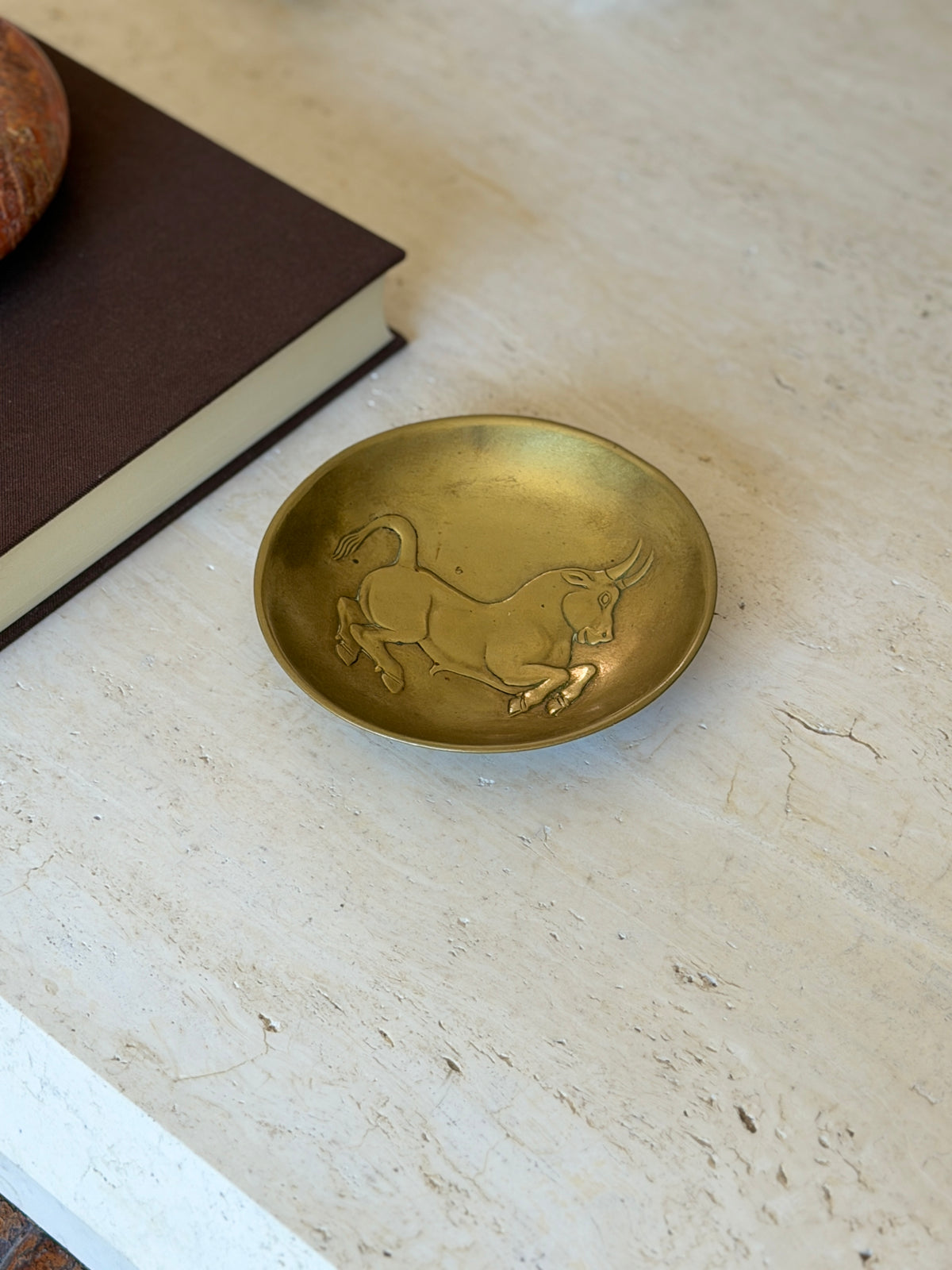 Riccardo Scarpa gilded bronze bowl with a leaping bull in low relief across the shallow well, on travertine beside a brown book
