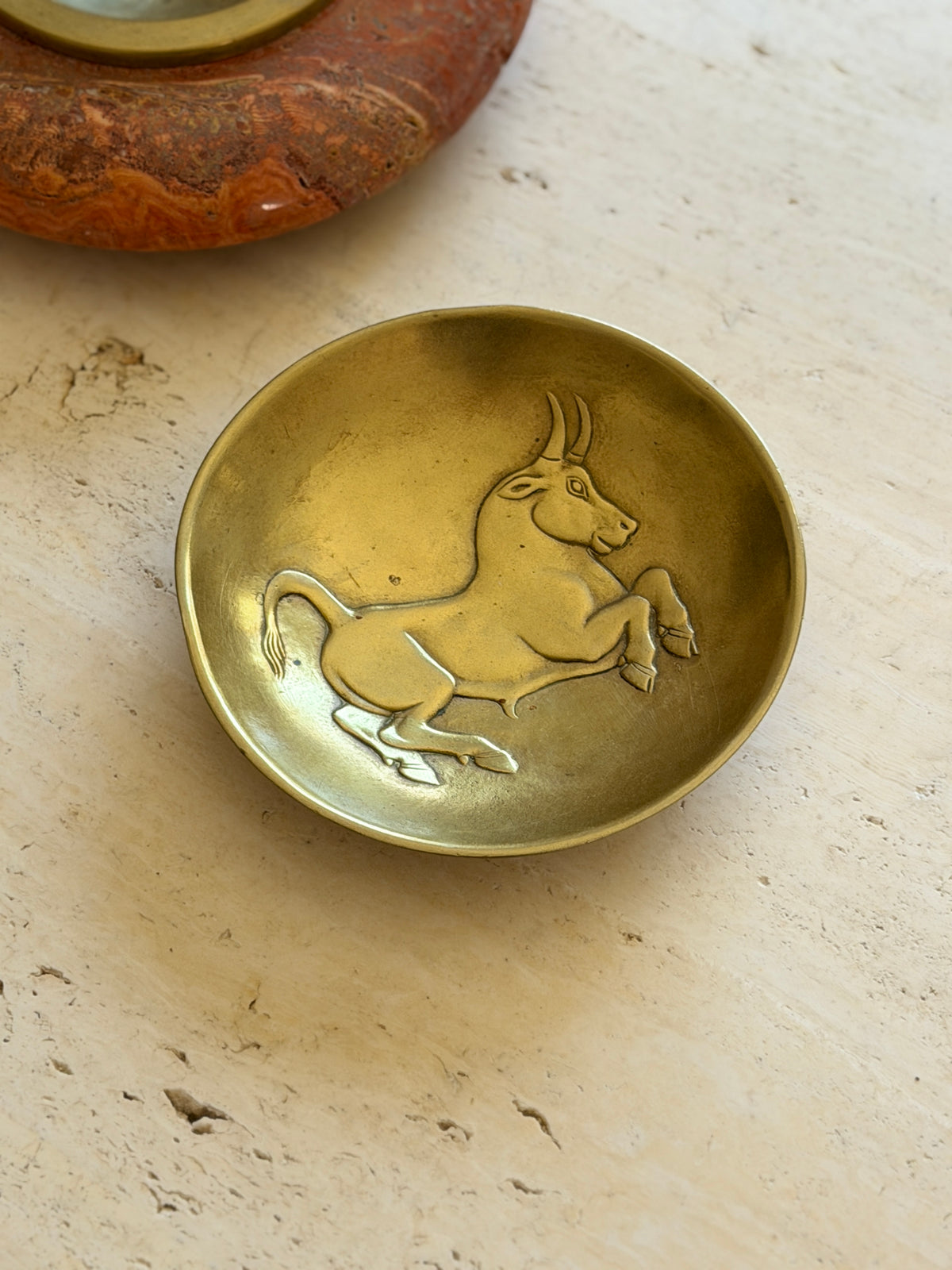 Close view of the bull relief in the Scarpa bowl beside a red stone ashtray, the animal rearing toward the rim