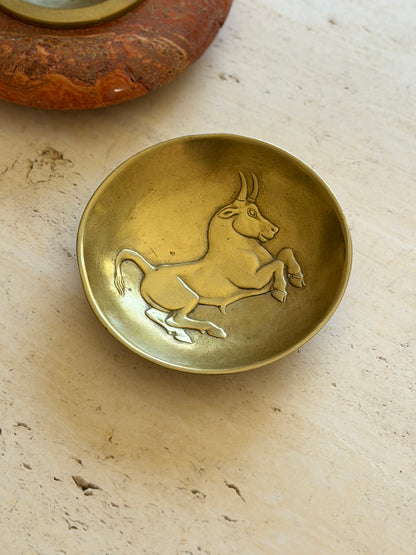 Close view of the bull relief in the Scarpa bowl beside a red stone ashtray, the animal rearing toward the rim