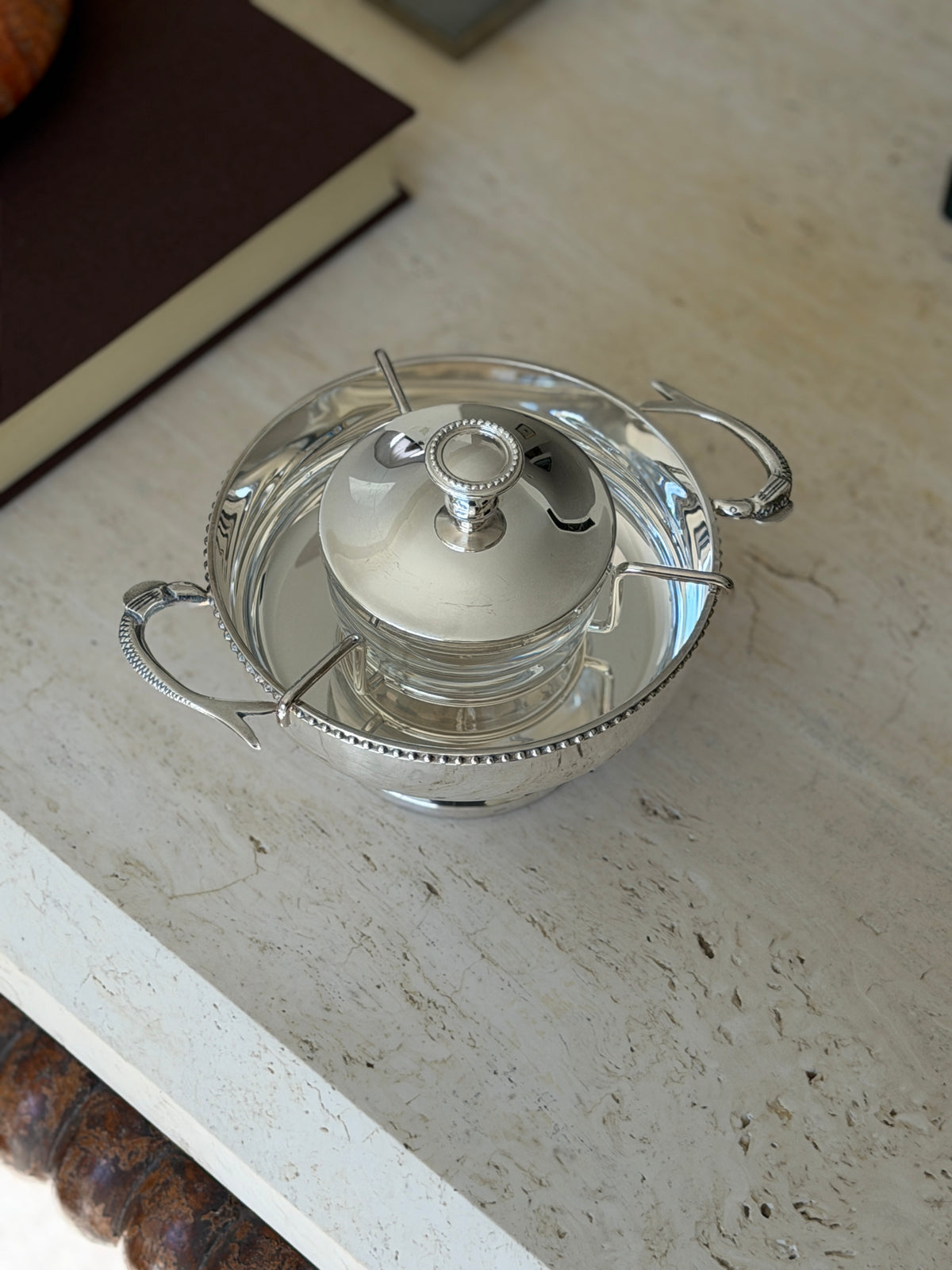 Overhead view of the Saint Hilaire silver plate caviar service, a lidded glass jar suspended in a beaded rim ice bowl with fish shaped handles