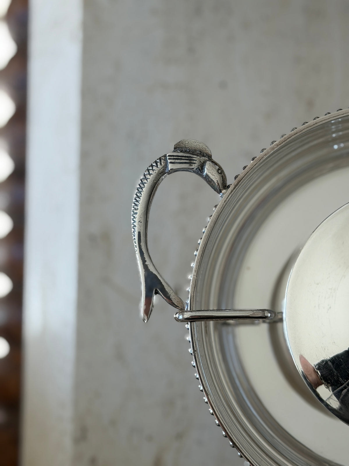 Close detail of a caviar server handle cast as a fish with crosshatched scales, its head meeting the beaded rim
