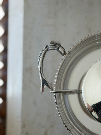 Close detail of a caviar server handle cast as a fish with crosshatched scales, its head meeting the beaded rim