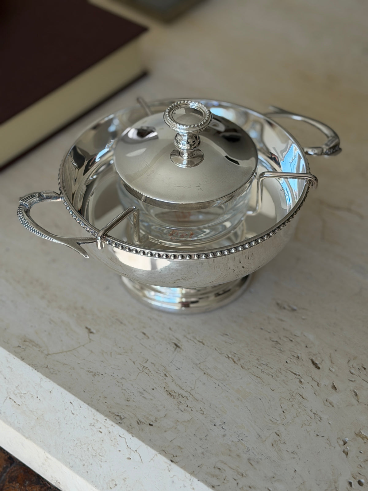 Three quarter view of the silver plate caviar service, showing the wire bracket holding the glass liner and the ring finial lid
