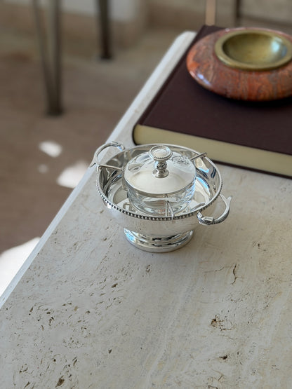 Caviar service on the corner of a travertine table beside a brown book and red stone ashtray, the pedestal foot visible