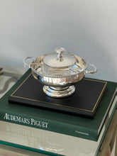 Saint Hilaire caviar service on a stack of books including Audemars Piguet, the polished bowl reflecting the room
