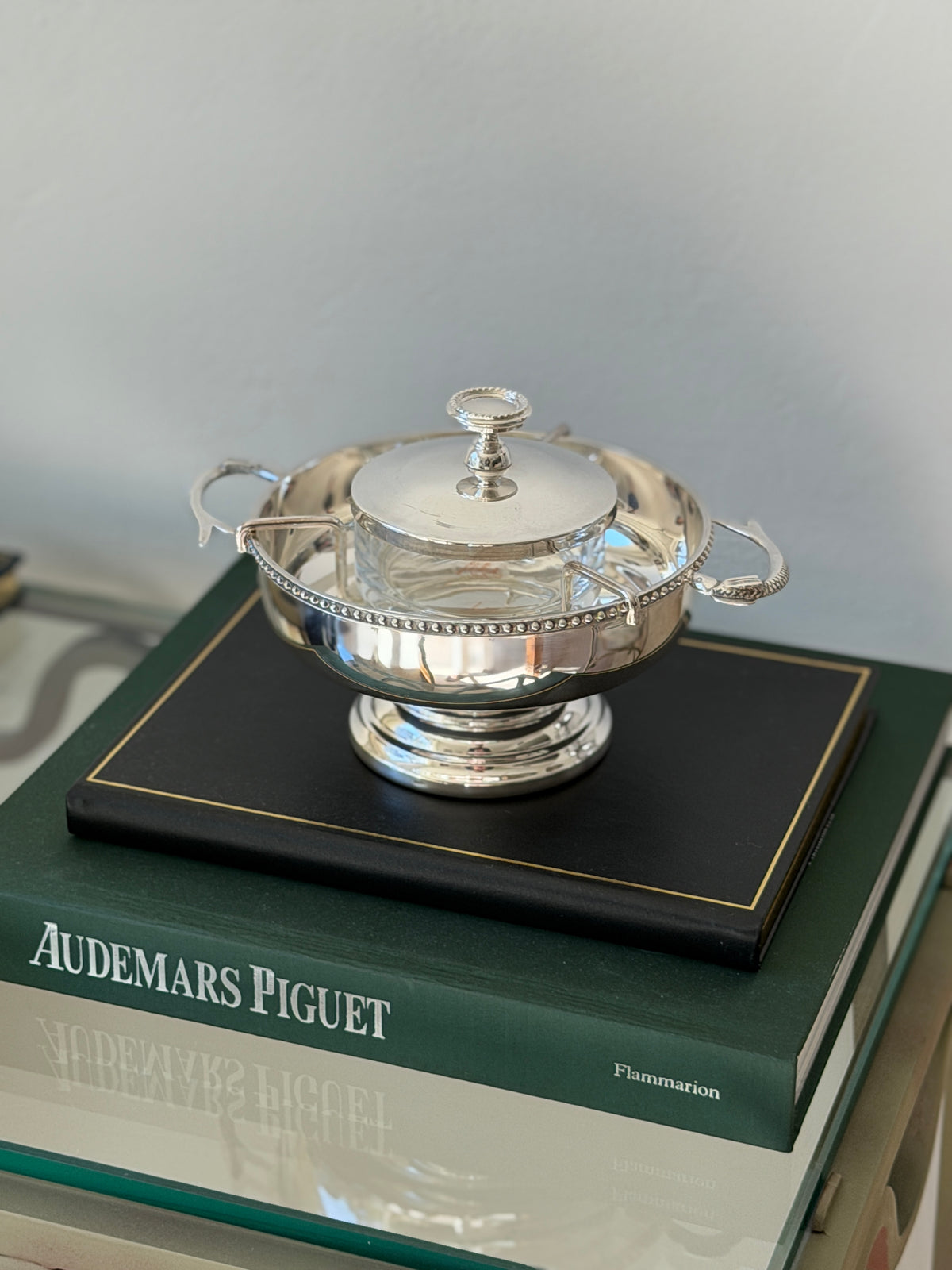 Saint Hilaire caviar service on a stack of books including Audemars Piguet, the polished bowl reflecting the room