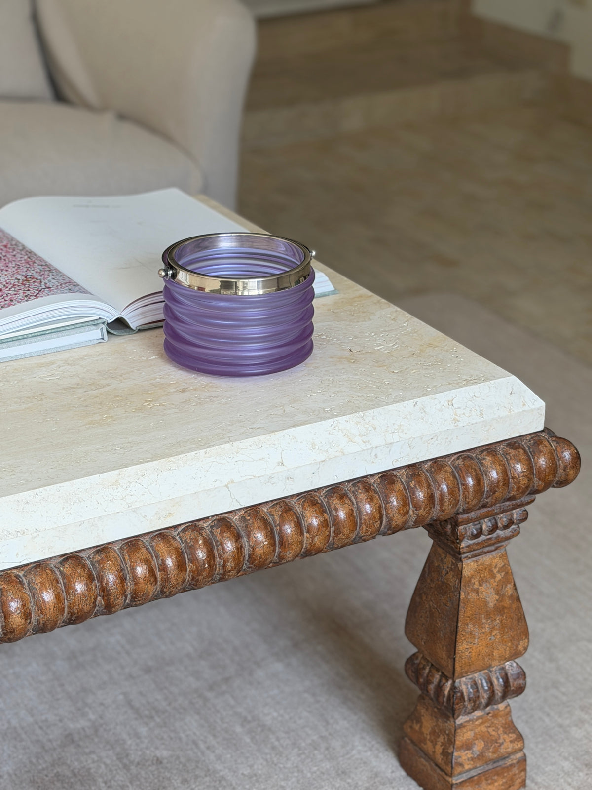 The bucket displayed on a stone-topped coffee table with a carved wooden leg, an open book beside it in a living room setting