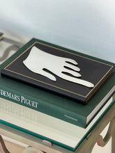 Side angle view of the flat hand sculpture on a stack of books, showing the thin sheet profile and curving fingers
