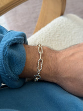 Bracelet worn on the wrist showing the clasp, wooden chair frame and cream cushion in the background