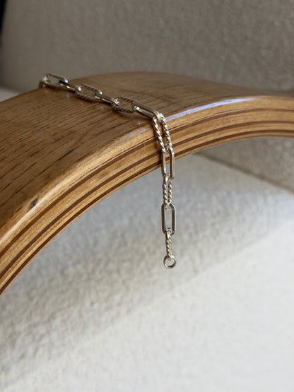Bracelet draped over the curved edge of a wooden chair arm, hanging loose against a cream carpet