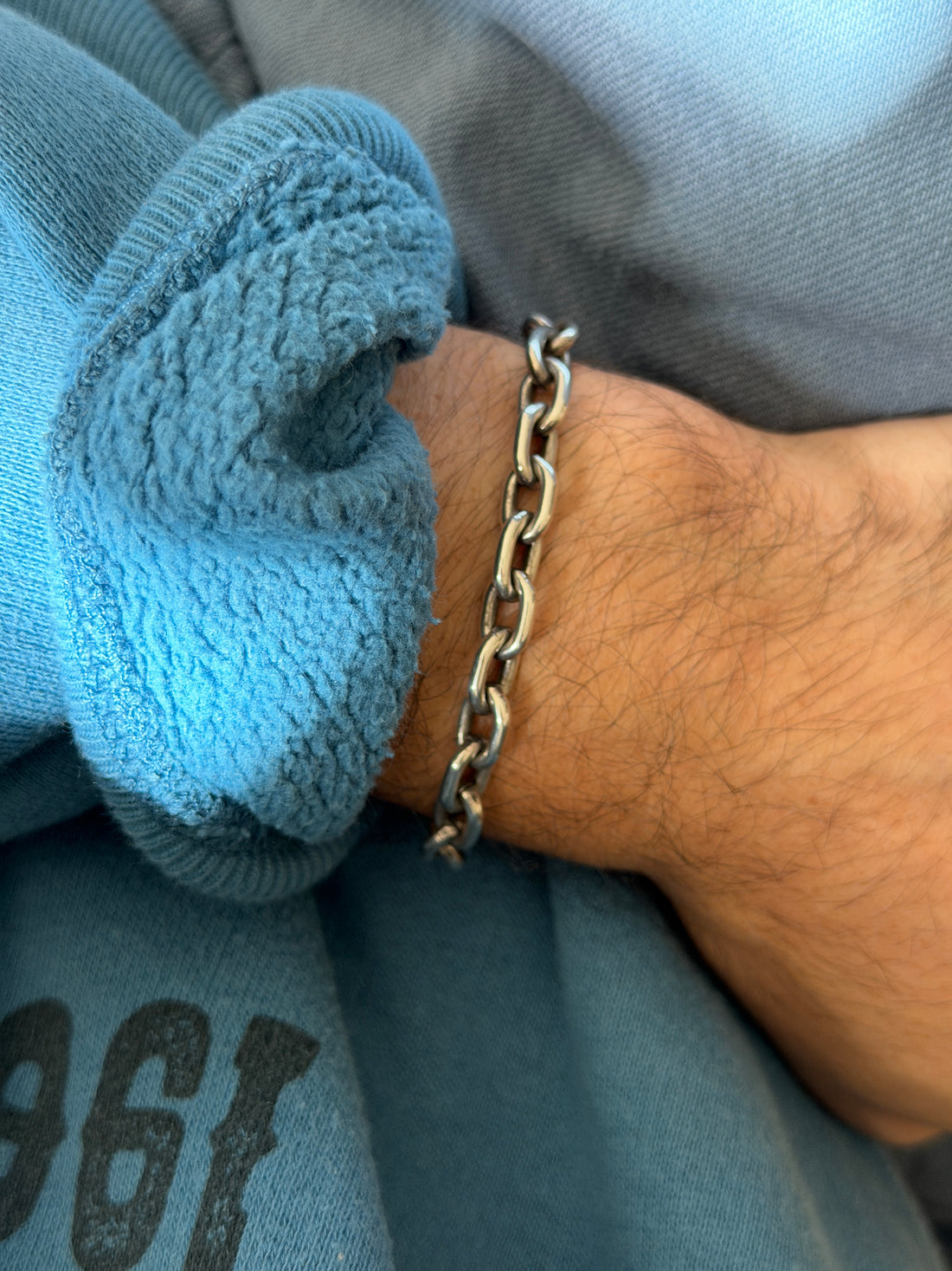 Heavy sterling silver oval link bracelet worn on the wrist against a blue fleece cuff, its thick links softly oxidized