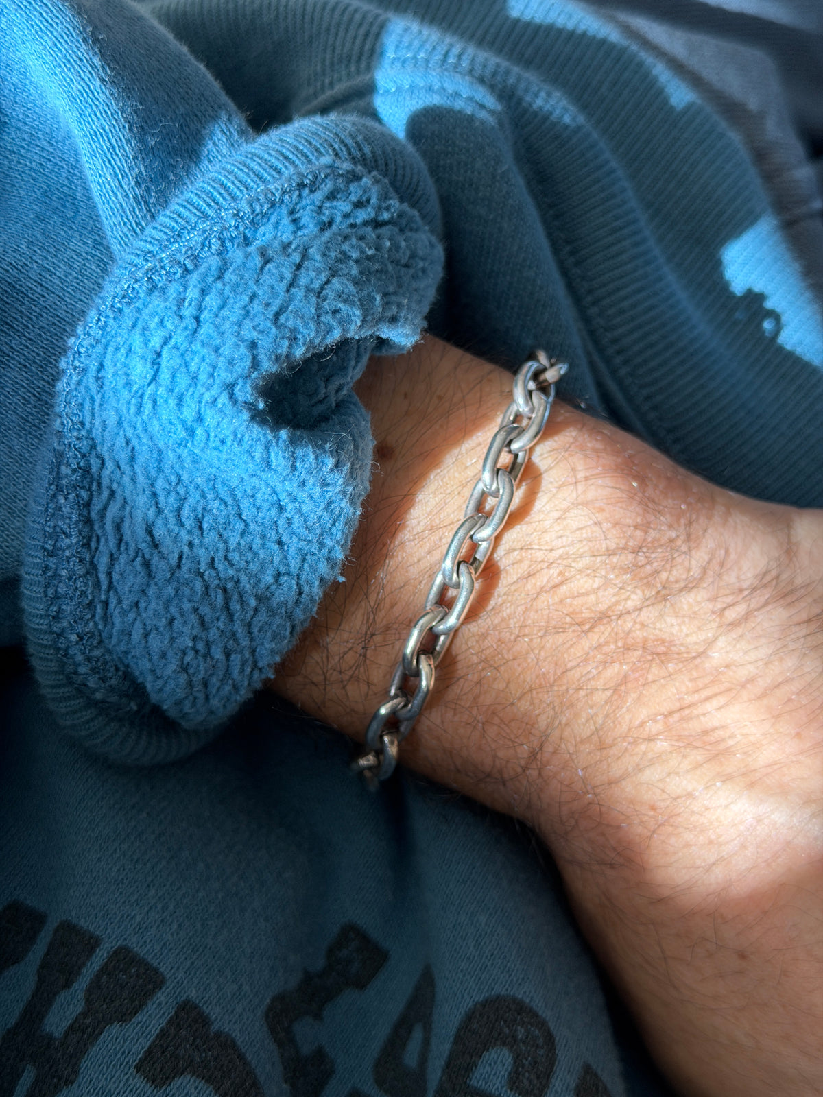 Heavy oval link biker bracelet on the wrist in bright sun, the chunky silver links casting shadows on the skin