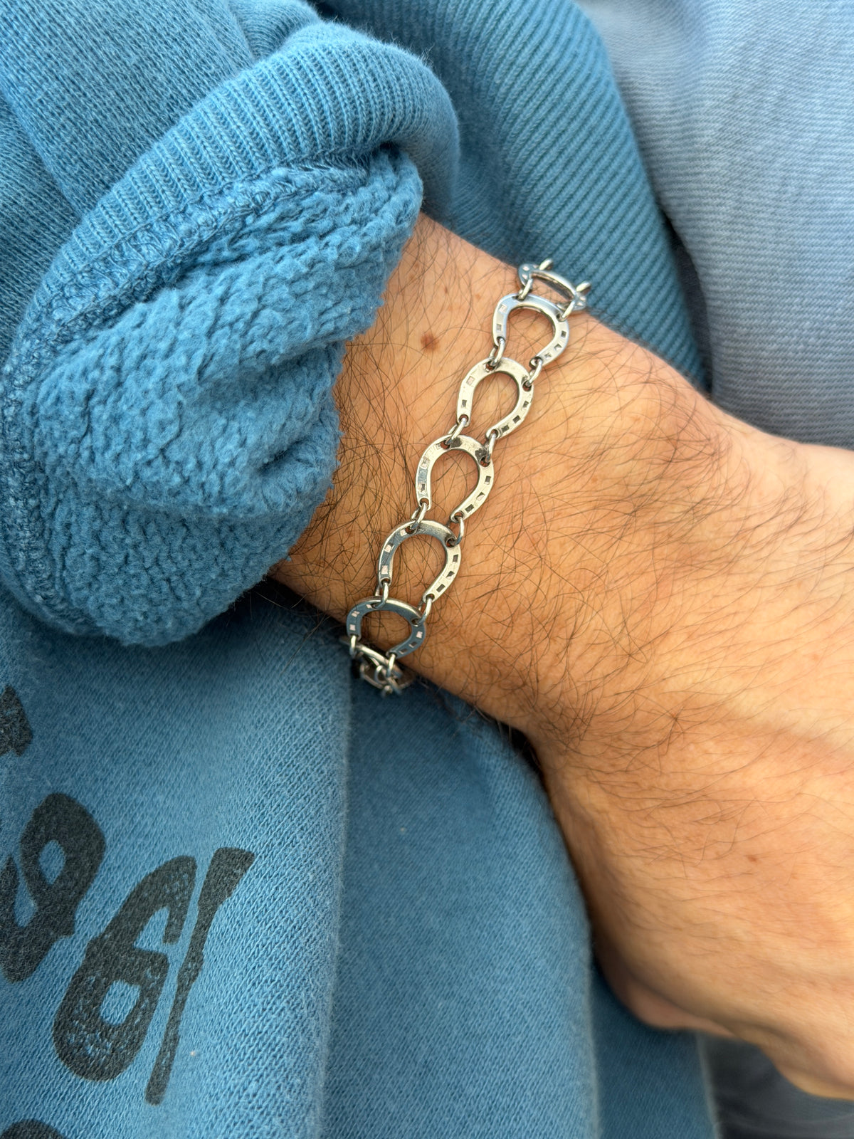 Straight on view of the horseshoe link bracelet worn over a blue sweatshirt, the stamped nail holes catching soft light