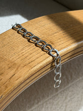Sterling silver horseshoe bracelet draped over a bentwood oak chair arm, a long run of linked horseshoes casting shadows