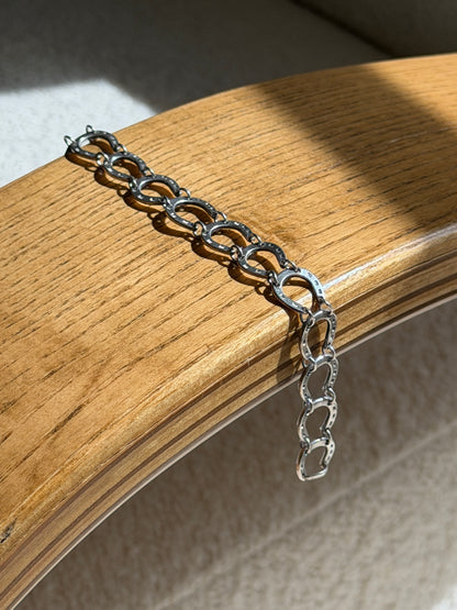 Sterling silver horseshoe bracelet draped over a bentwood oak chair arm, a long run of linked horseshoes casting shadows