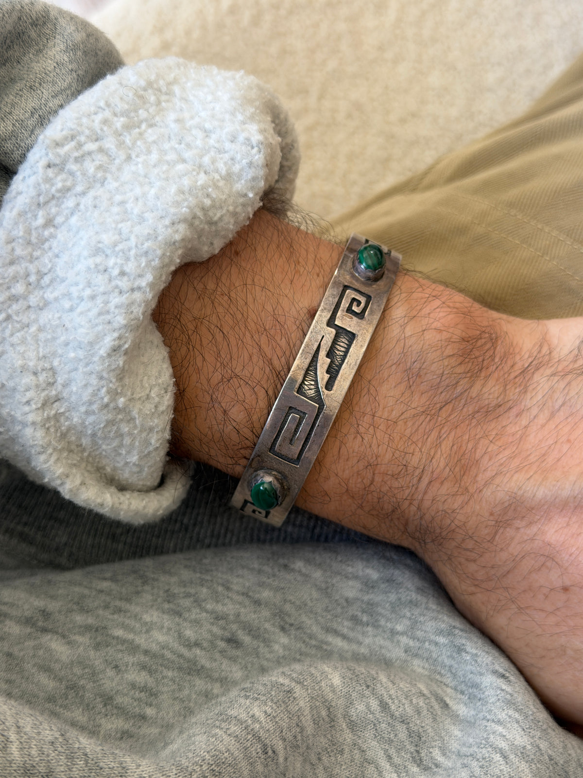 Sterling silver cuff with overlay style meander and stepped motifs on an oxidized background, set with two oval malachite cabochons, worn on the wrist