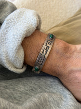 Sterling silver cuff with overlay style meander and stepped motifs on an oxidized background, set with two oval malachite cabochons, worn on the wrist