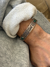 Angled view of the Native American motif cuff, the darkened cutout design contrasting with the brushed silver surface