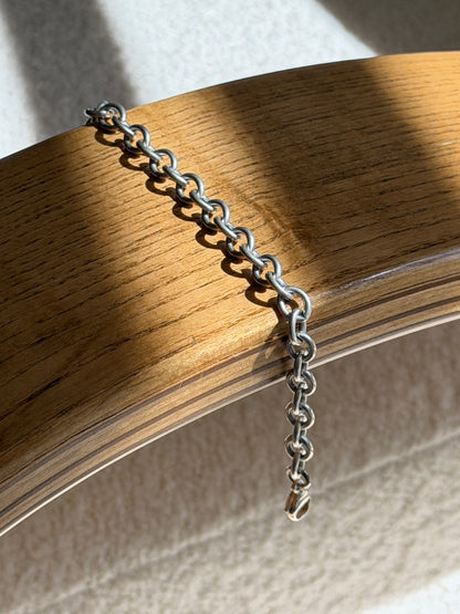 Chunky open link bracelet draped over a bentwood oak chair arm, ending in a silver lobster clasp