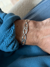 Sterling silver bracelet of engraved oval links, each overlapping a smaller ring in a figure eight, worn on the wrist