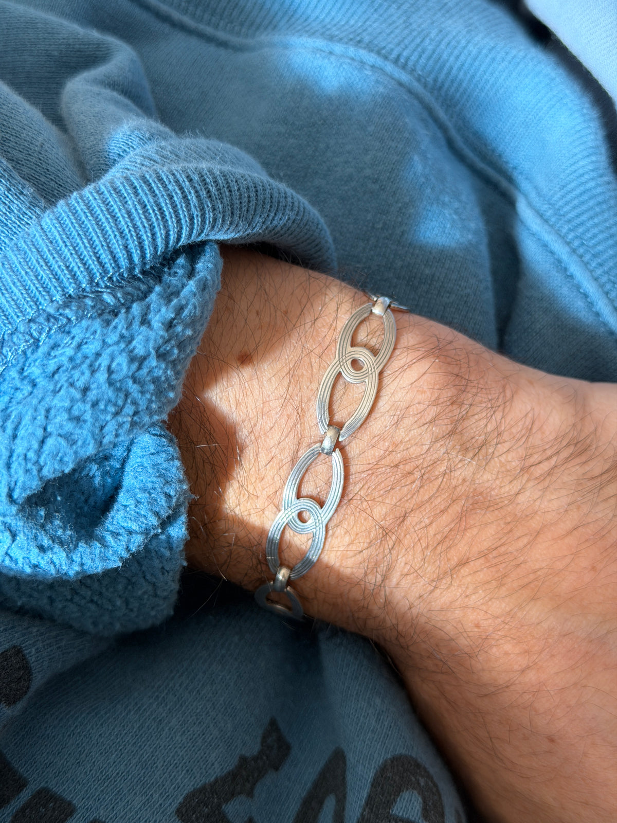 Figure eight link bracelet on the wrist in sunlight, fine engraved lines tracing each oval and inner ring