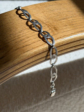 Sterling silver figure eight link bracelet draped over a bentwood oak chair arm, ending in a box clasp