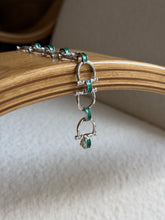 Angled view of the green enamel bit bracelet styled on a jewelry stand