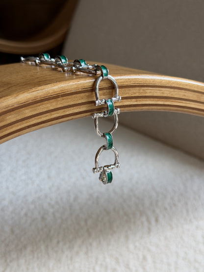 Angled view of the green enamel bit bracelet styled on a jewelry stand