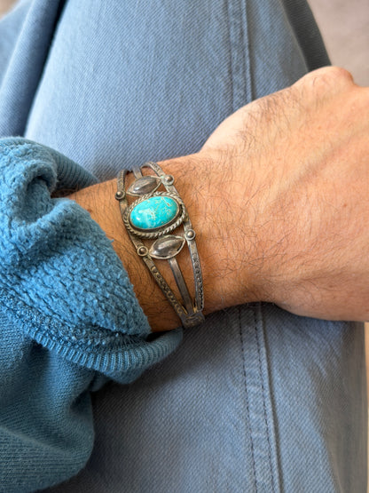 Triple band turquoise cuff worn on the wrist, the stone showing brown matrix veining and the side bands stamped with arc patterns