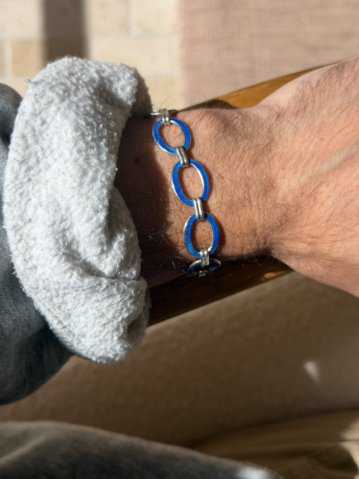 Side view of the sterling and blue enamel link bracelet worn over a wooden chair arm, polished silver rims framing each open oval