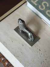 Overhead angled view of the pewter lion figure on a table beside a green book, facing upward with tail extending to the side