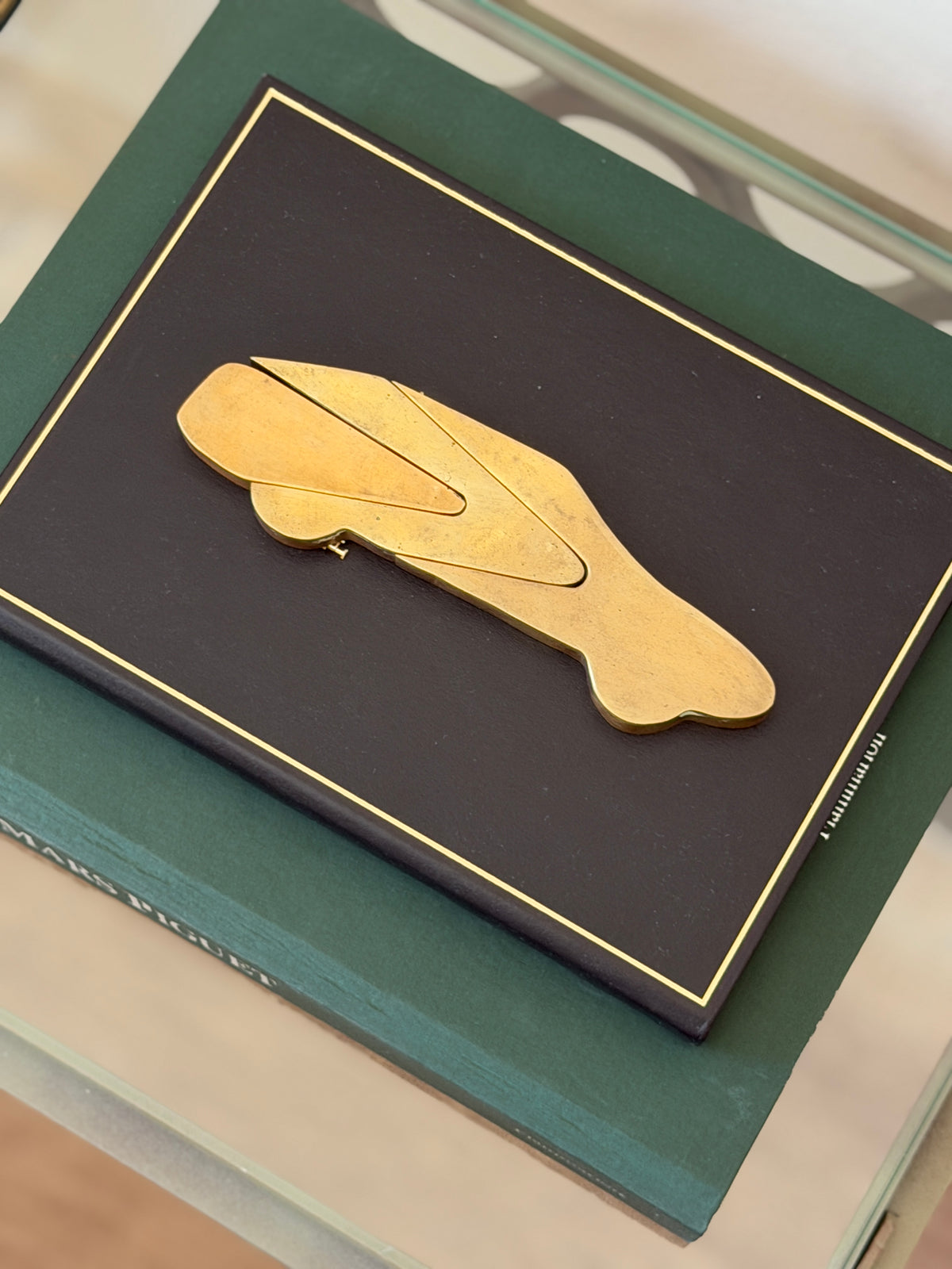 Side silhouette view of vintage interlocking bronze car puzzle paperweight resting on green book