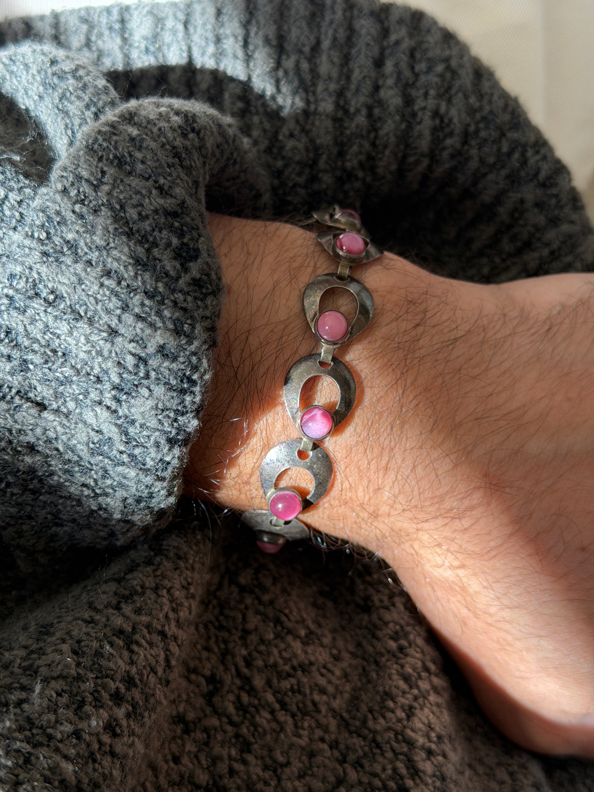 Hermann Siersbol Danish sterling silver bracelet of curved open links, each set with a round pink cabochon, worn on the wrist against a gray knit sleeve