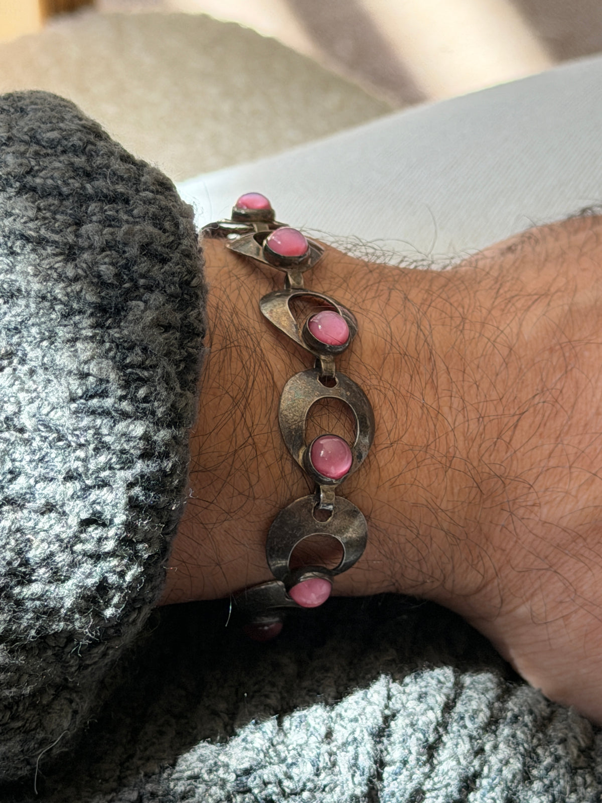 Close wrist view of the Siersbol bracelet, the oxidized silver links curving around bezel set pink stones