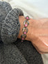 Pink cabochon bracelet worn over a gray sweater cuff, the hinged links and darkened patina along each curved panel