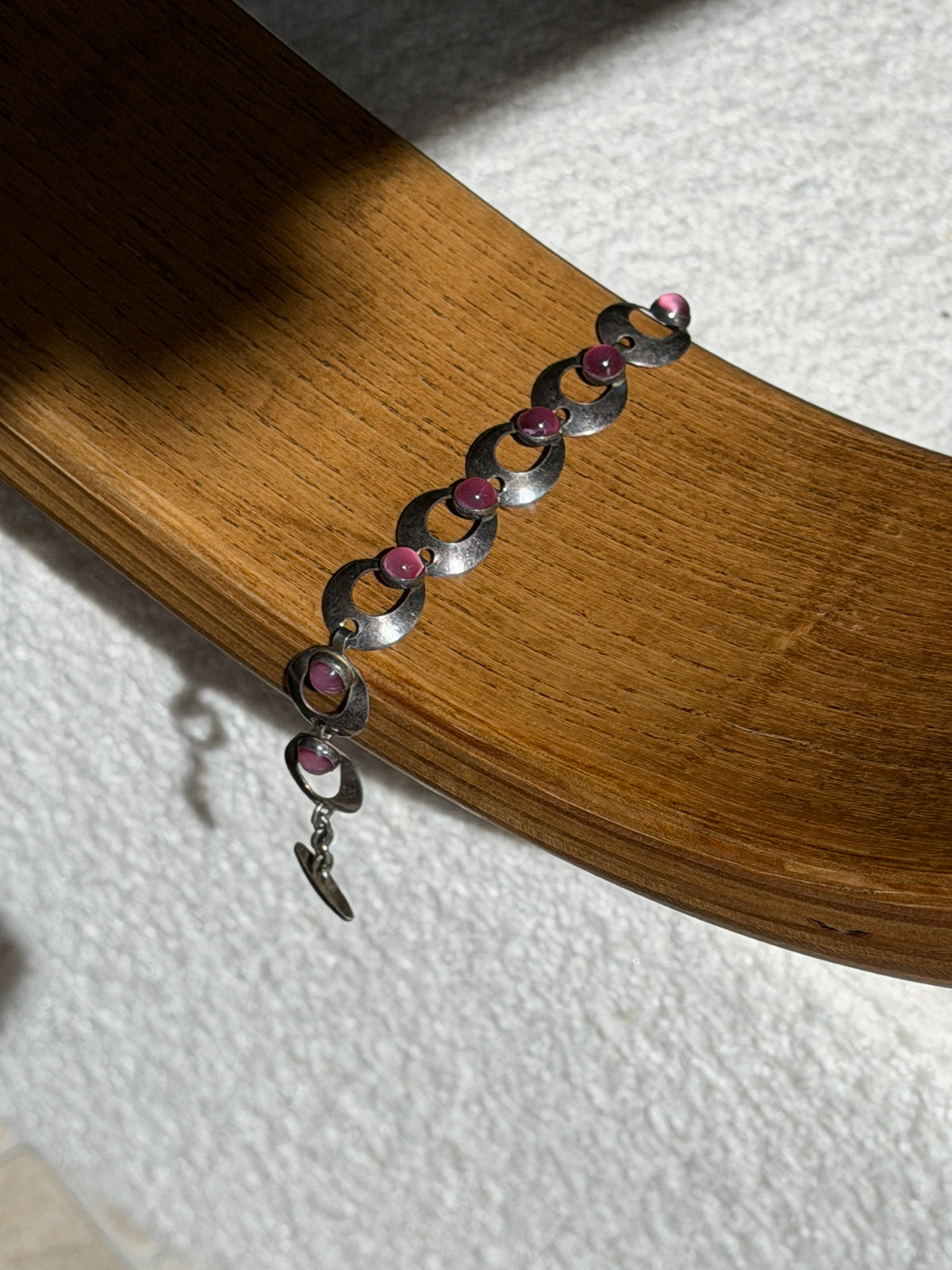 Hermann Siersbol pink cabochon bracelet draped over a bentwood oak chair arm, showing the full run of links and the hook clasp