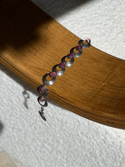 Hermann Siersbol pink cabochon bracelet draped over a bentwood oak chair arm, showing the full run of links and the hook clasp