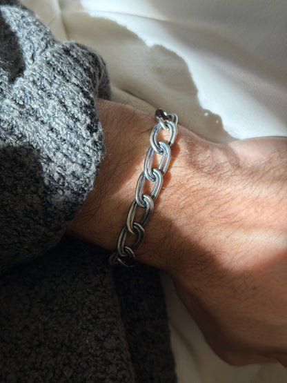 Sterling double oval link bracelet on the wrist in raking sunlight, polished edges against the oxidized grooves