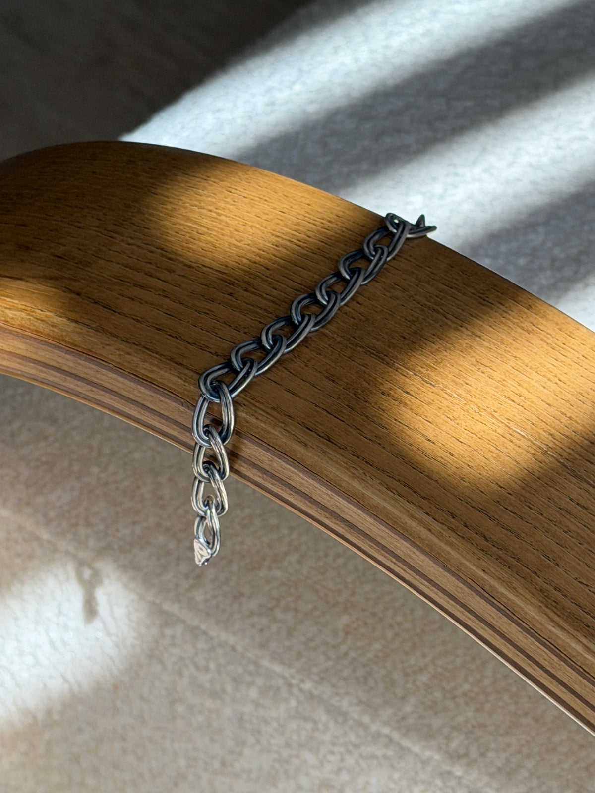 Italian double oval link bracelet draped over a bentwood oak chair arm in striped sunlight, the clasp end hanging free