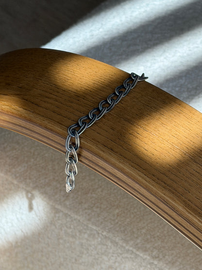 Italian double oval link bracelet draped over a bentwood oak chair arm in striped sunlight, the clasp end hanging free