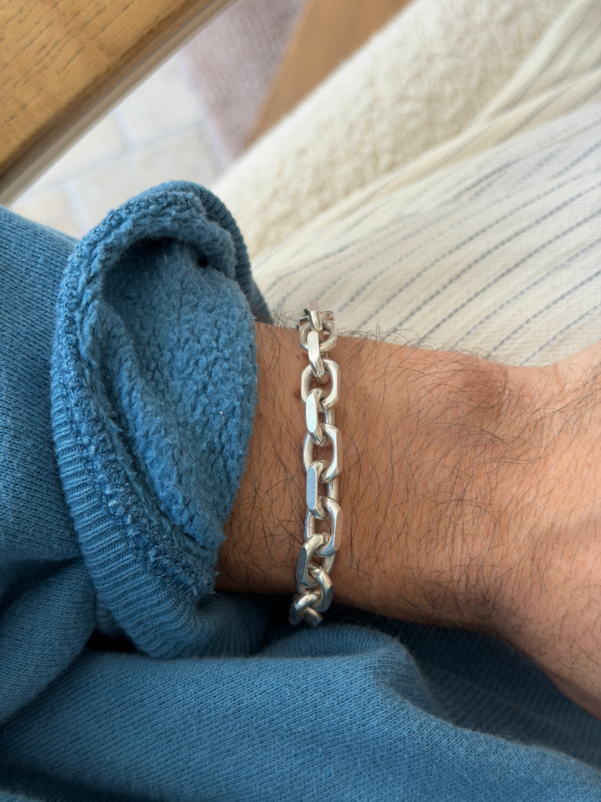 Bracelet worn on the wrist near a wooden table edge and cream cushion