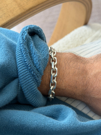 Bracelet draped over the curved edge of a wooden chair arm, hanging loose against a cream carpet