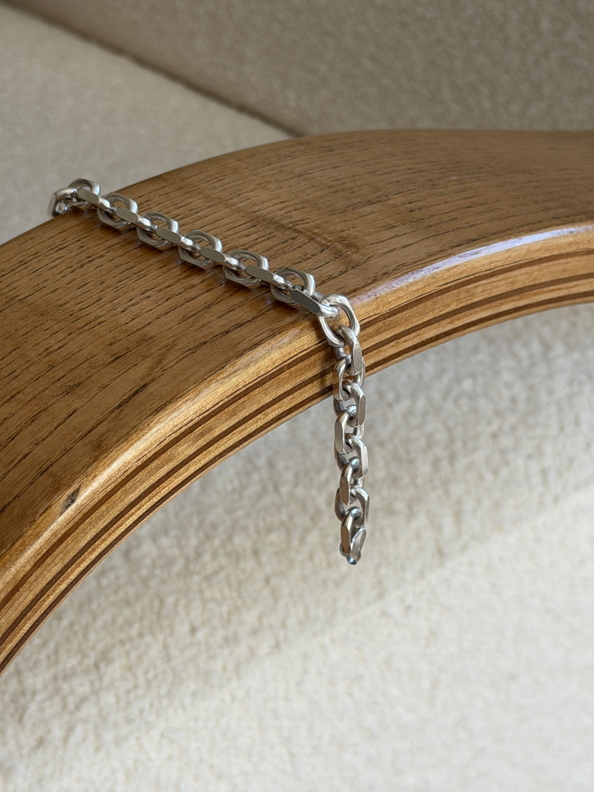 Closer view of the draped bracelet showing the clasp and geometric link detail against the wood edge