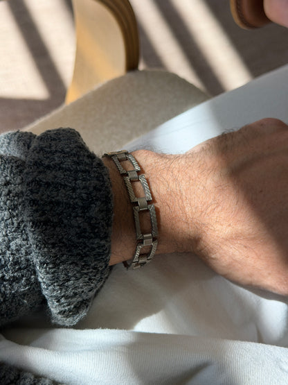 Panel link bracelet worn on the wrist near a bentwood chair, the open rectangles and barrel connectors in raking light