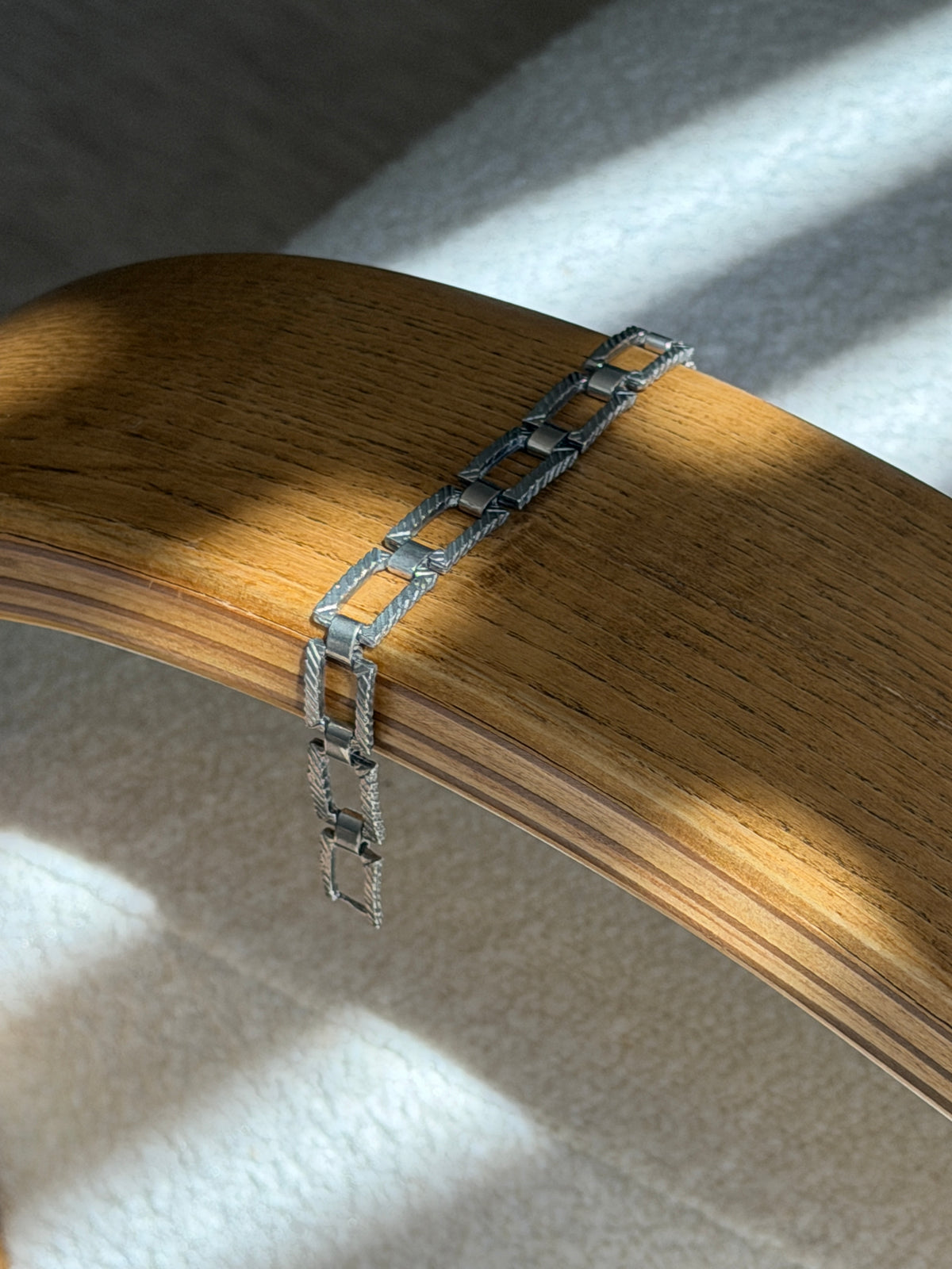 Sterling silver panel bracelet draped over a bentwood oak chair arm, the engraved rectangular links hanging free at one end